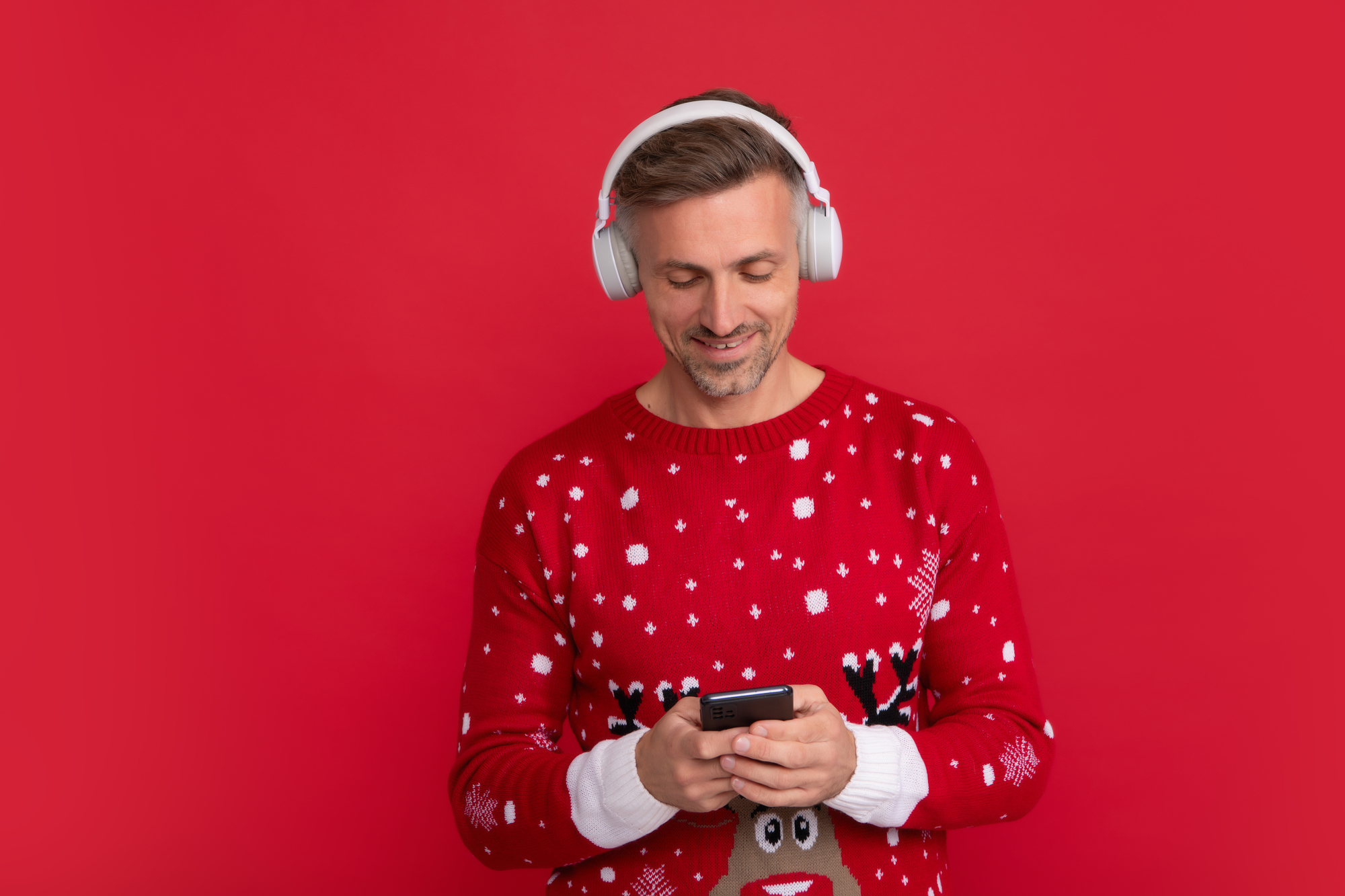 Homme en pull de Noël écoutant musique avec un casque audio Bluetooth reçu à Noël